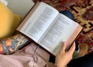 A tattooed man reads a Bible.